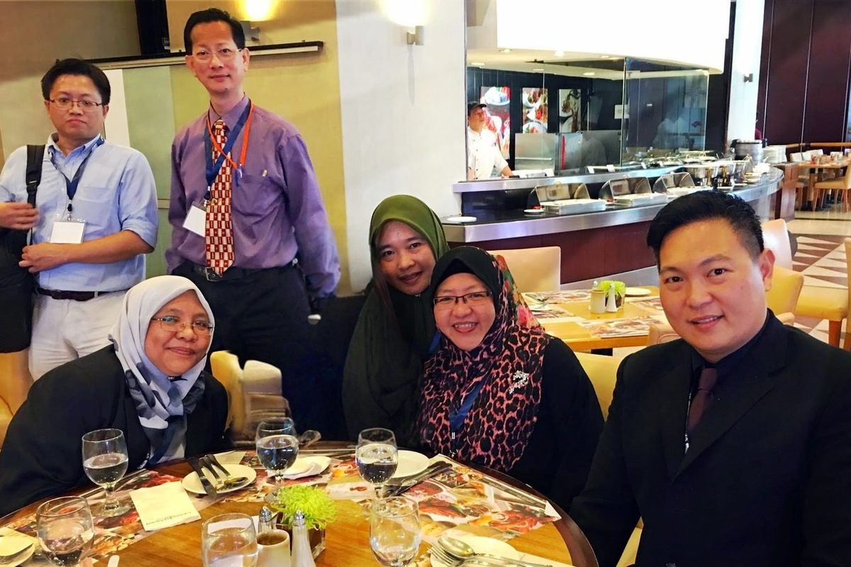 Six conference delegates seated and standing around a lunch table at the hotel