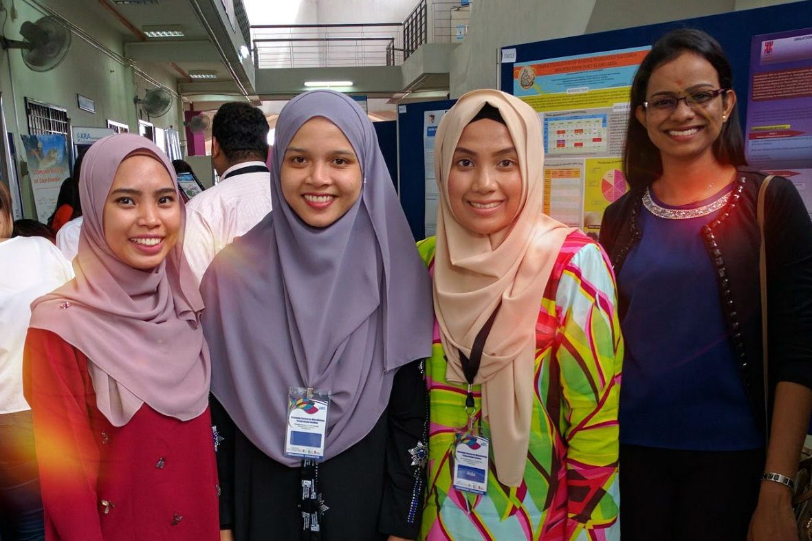 Four smiling delegates stand together in front of research posters