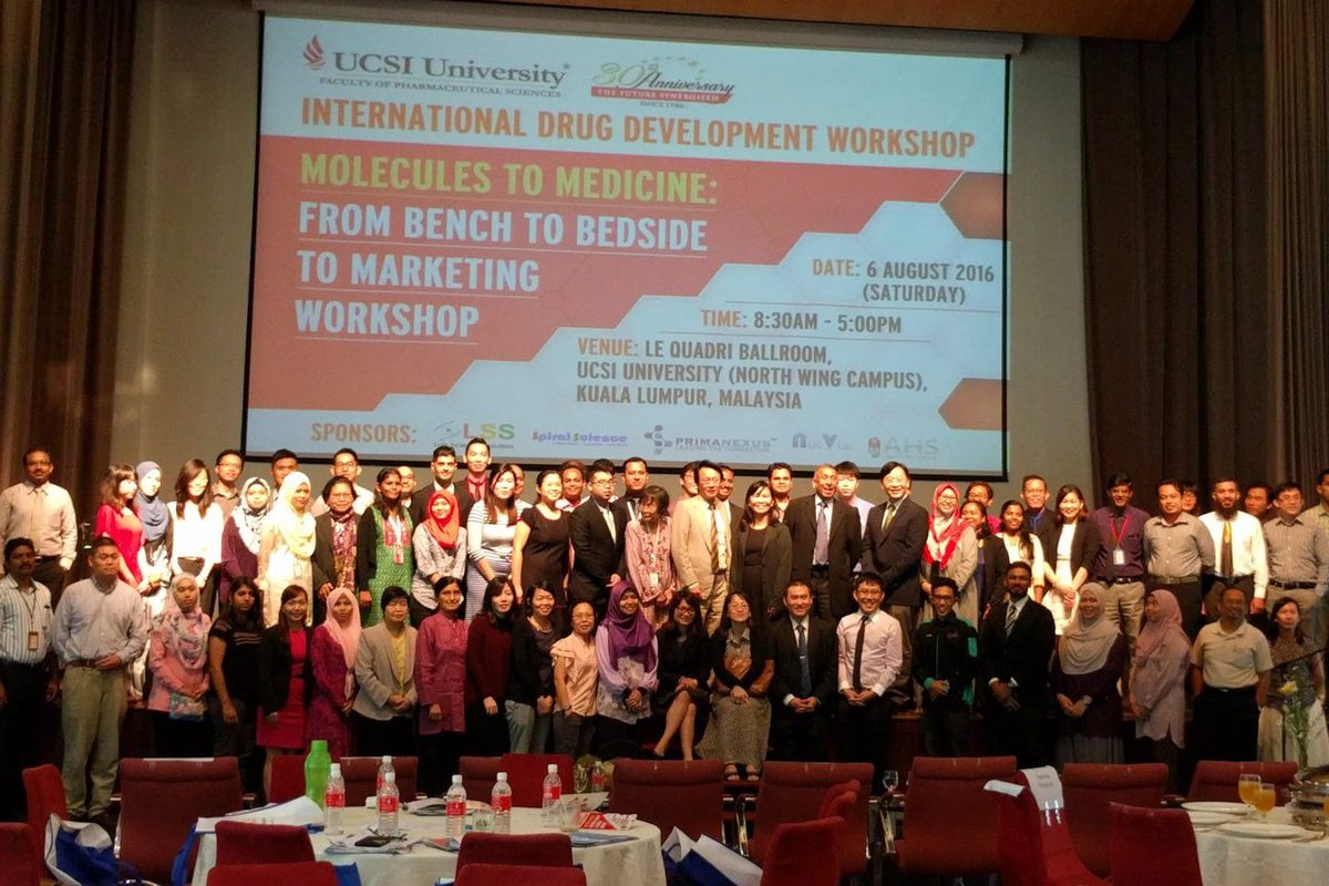 Large group of workshop participants on stage in front of a screen showing the workshop title and sponsors