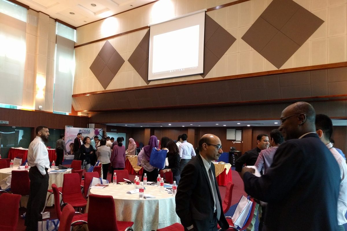 Participants standing and talking between round tables in the ballroom, with a refreshment table at the back