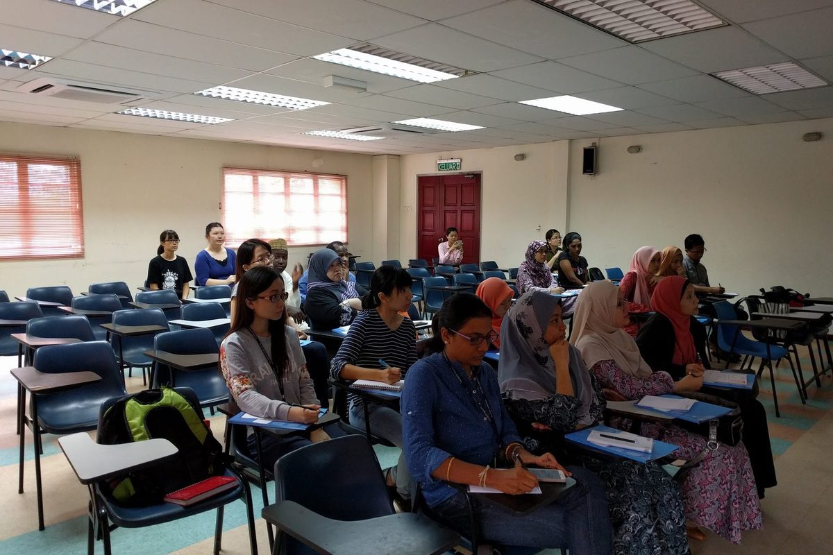 Participants seated at desks in a bright seminar room, some taking notes, during the workshop.