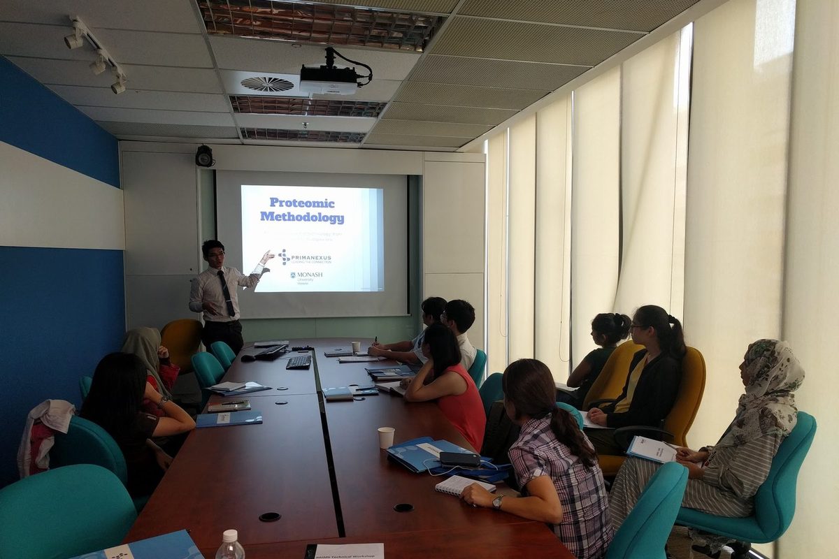 Participants around a conference table listening to a speaker beside a slide titled Proteomic Methodology