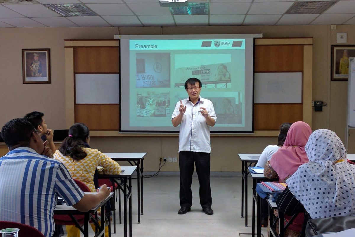 A speaker presents to seated participants in front of a projected slide