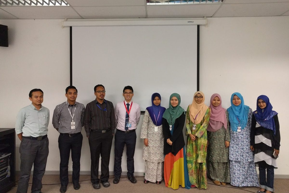 A group of ten people standing in a row in front of a projection screen