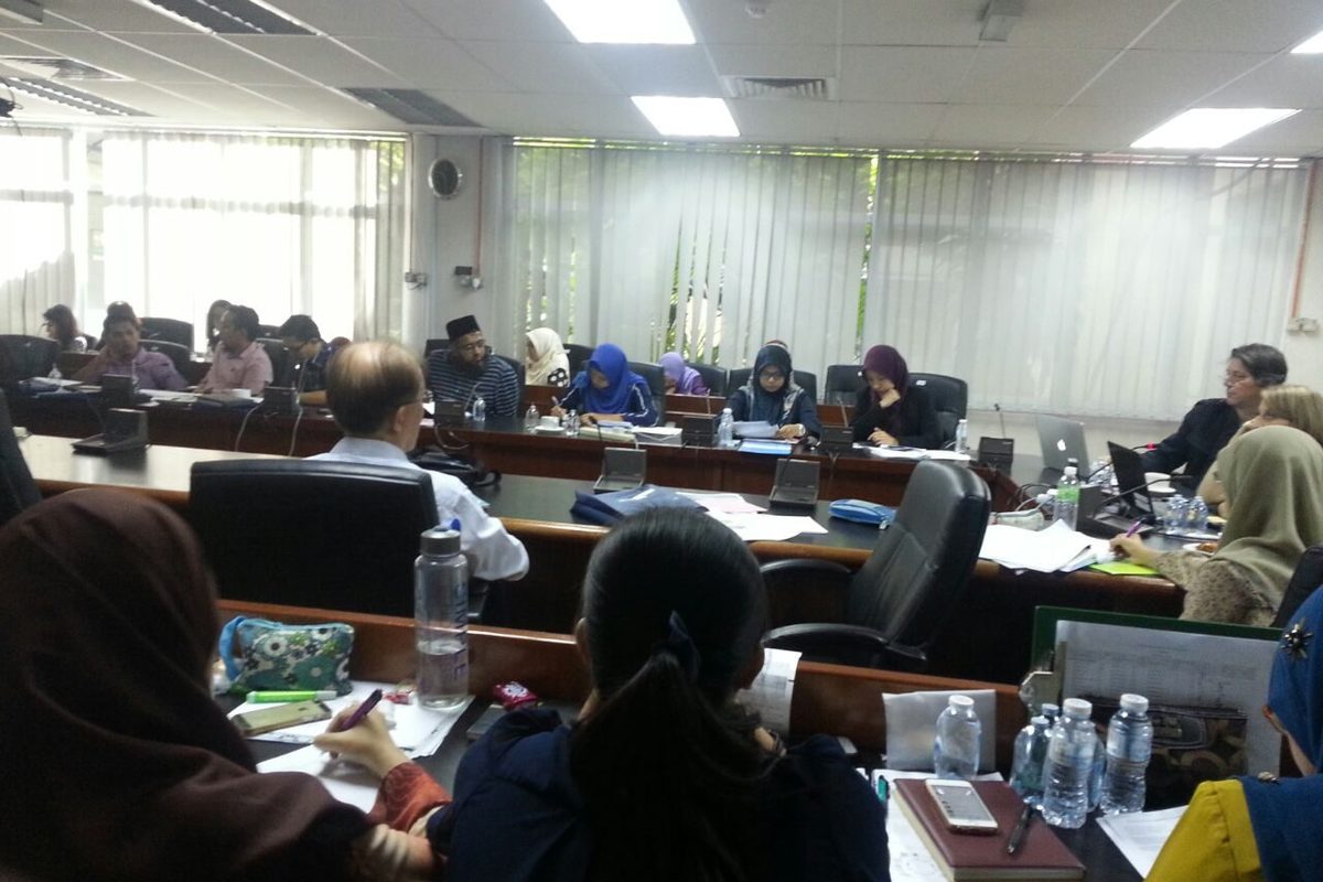 Participants taking notes at long desks with laptops and notebooks during a workshop session