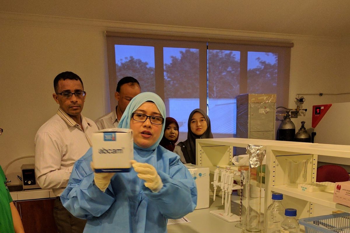 A trainer in a blue lab gown and gloves holds up an Abcam ELISA kit box in the laboratory