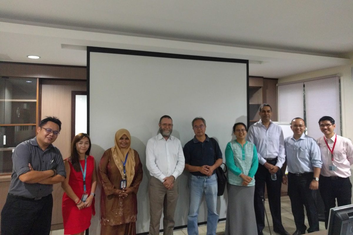 Members and guests stand in a row for a group photo in a meeting room, in front of a screen