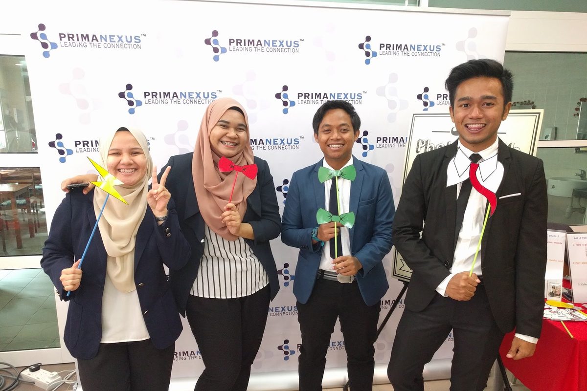 Four participants pose with photo props at the Prima Nexus photo wall