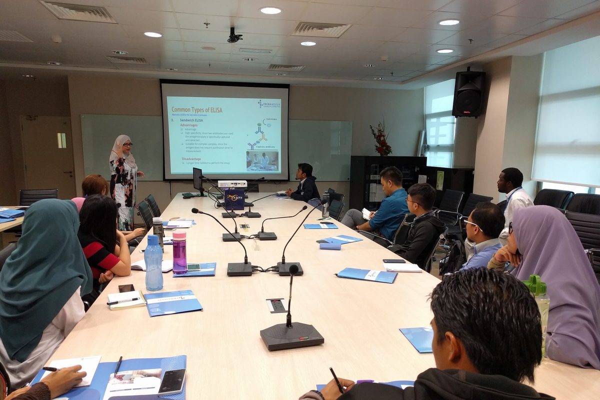 A presenter explains a slide on common types of ELISA to participants seated around a meeting table
