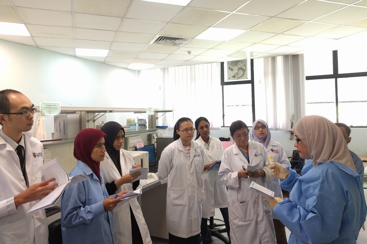 Participants in lab coats gather around a trainer in the laboratory