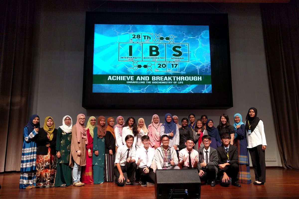 Participants pose for a group photo on stage under a large screen showing the IBS 2017 seminar logo