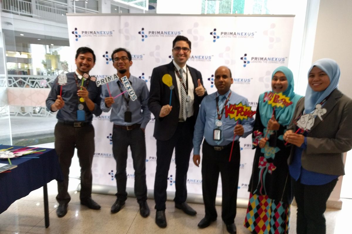 Six participants holding photo props in front of the Prima Nexus backdrop