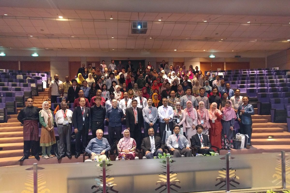 Large group photo of conference participants on the tiered seats of a lecture hall, front row seated