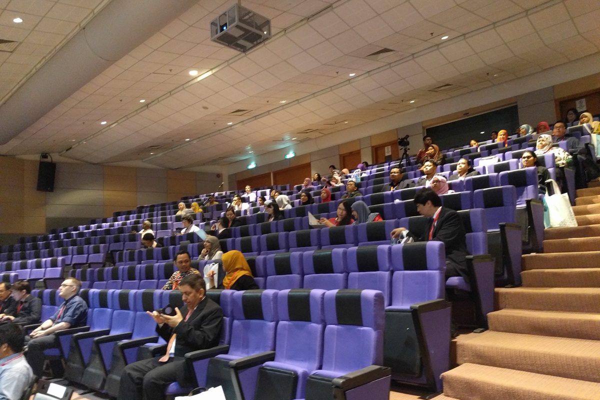 Delegates seated in a tiered lecture hall with purple seats
