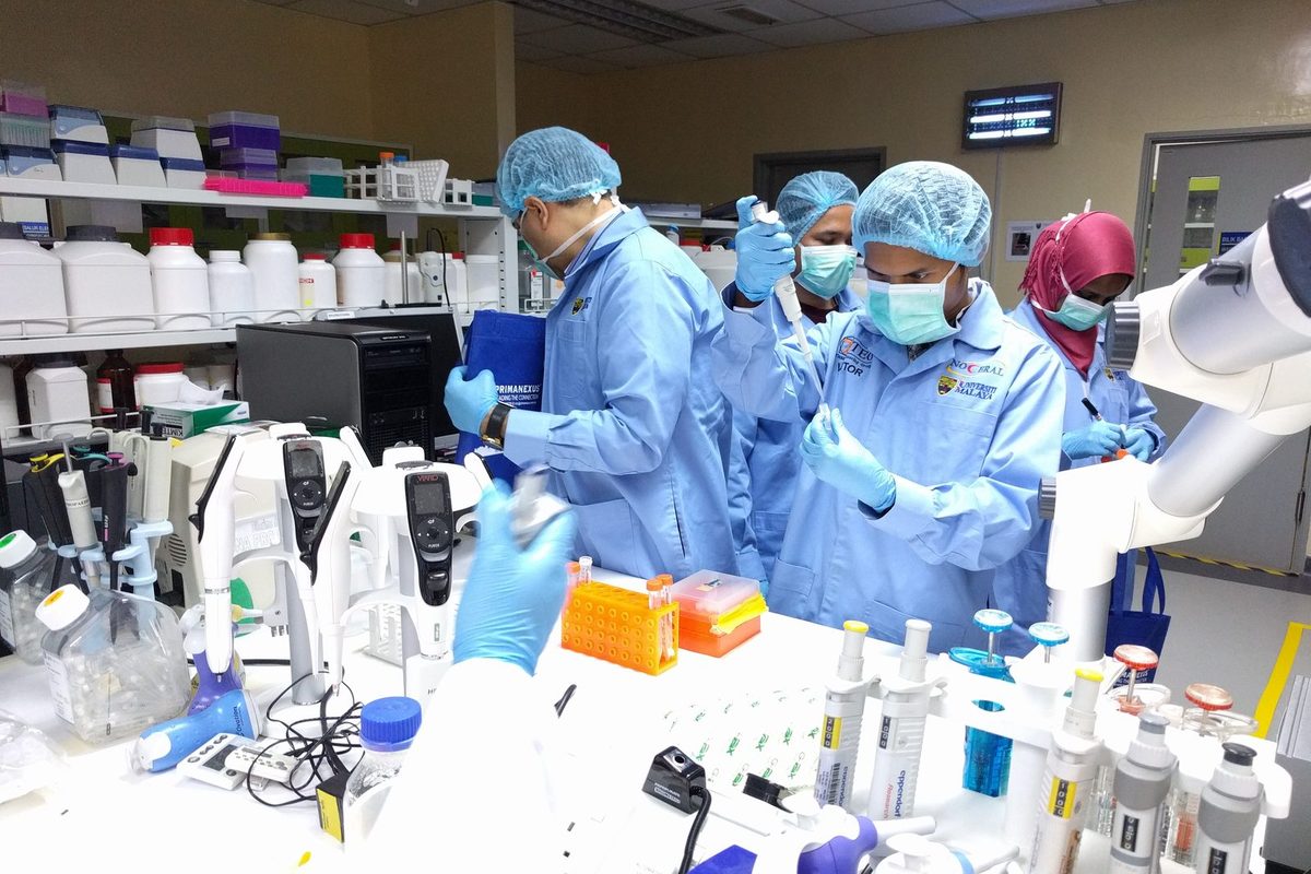 Participants in blue lab coats use pipettes at a laboratory bench