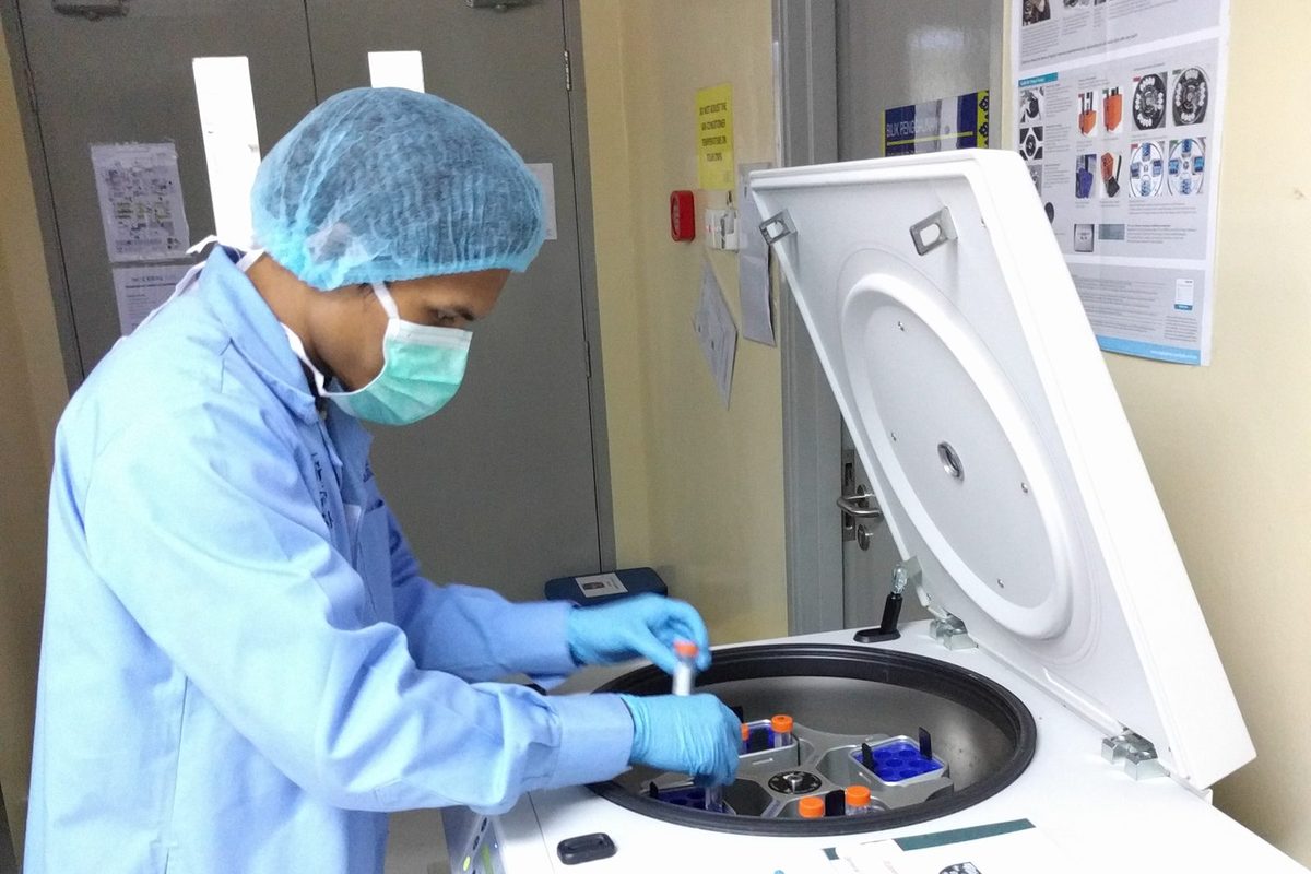 A participant in a lab coat loads sample tubes into a benchtop centrifuge