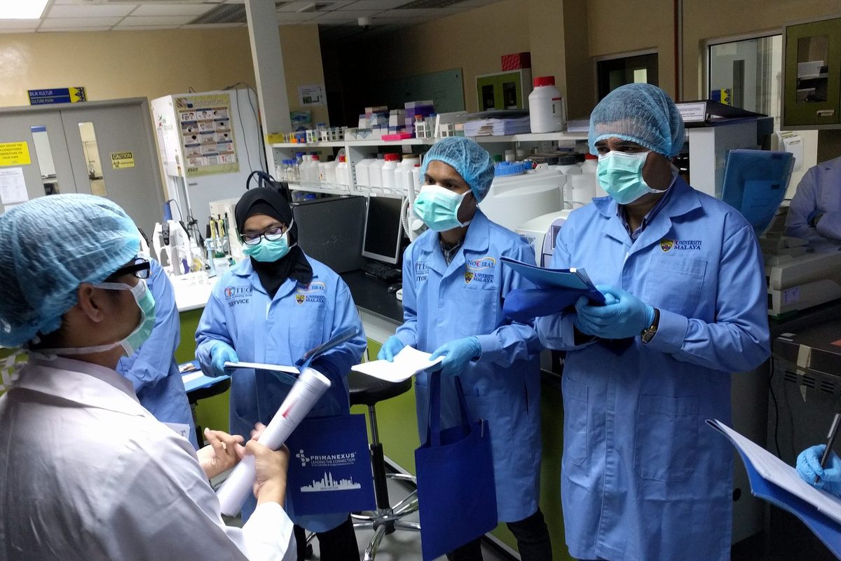 Participants in blue lab coats hold papers during a briefing in the laboratory