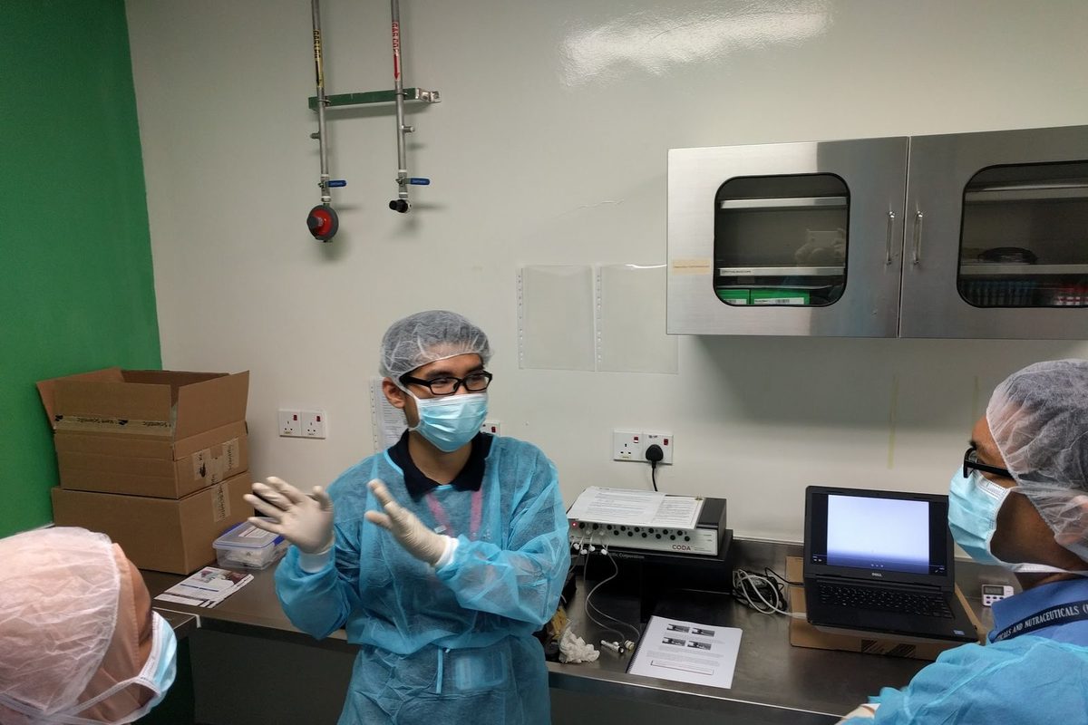 A trainer in gown and mask explains the CODA controller and laptop on a stainless steel bench