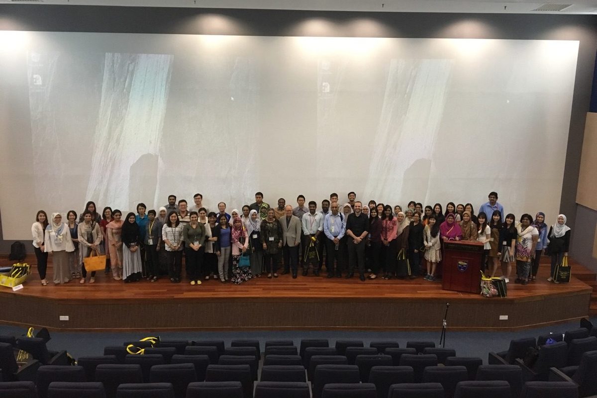 Course participants standing together on the auditorium stage for a group photo, rows of empty seats in front