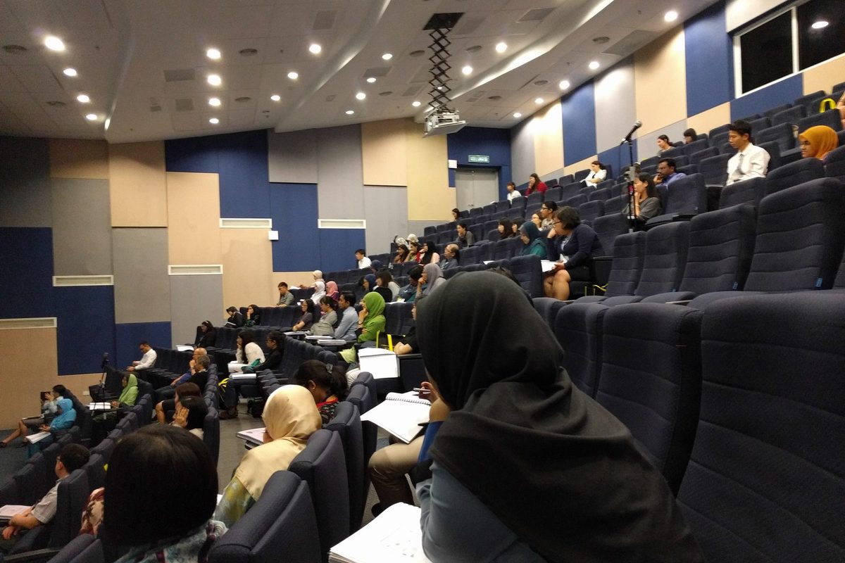 Delegates seated across the tiered auditorium with notes on their laps during a session