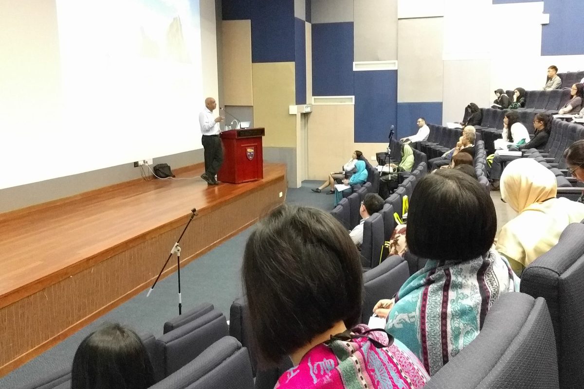 View from the audience of a lecturer at the podium beside a large projection screen