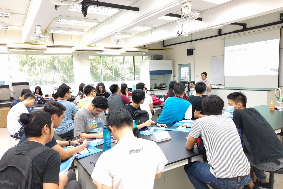 Participants with notes at laboratory benches while the speaker talks at the front of the room