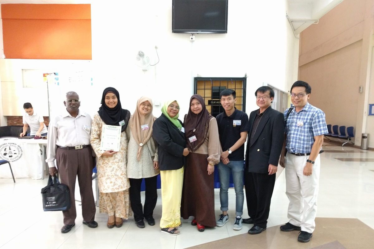 Participants and speakers stand together in a hall, some holding papers