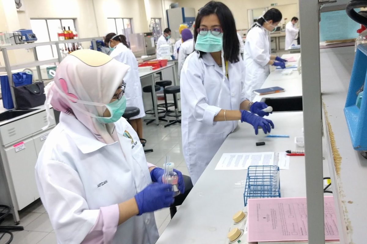 Two participants in lab coats, gloves and masks at work at a laboratory bench
