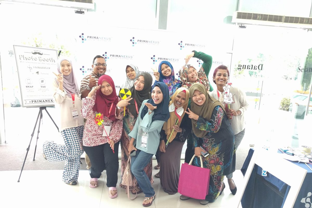 A group of delegates posing with props in front of the Prima Nexus photo booth backdrop