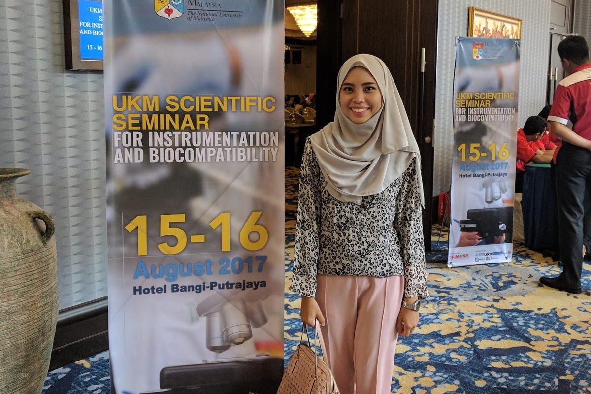 A participant stands beside the seminar banner at the entrance to the hall