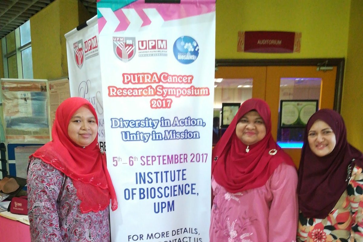 Three delegates stand beside the Putra Cancer Research Symposium 2017 banner at the Institute of Bioscience, UPM
