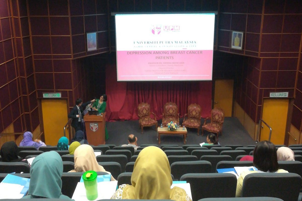 Delegates seated in the auditorium facing the stage and screen