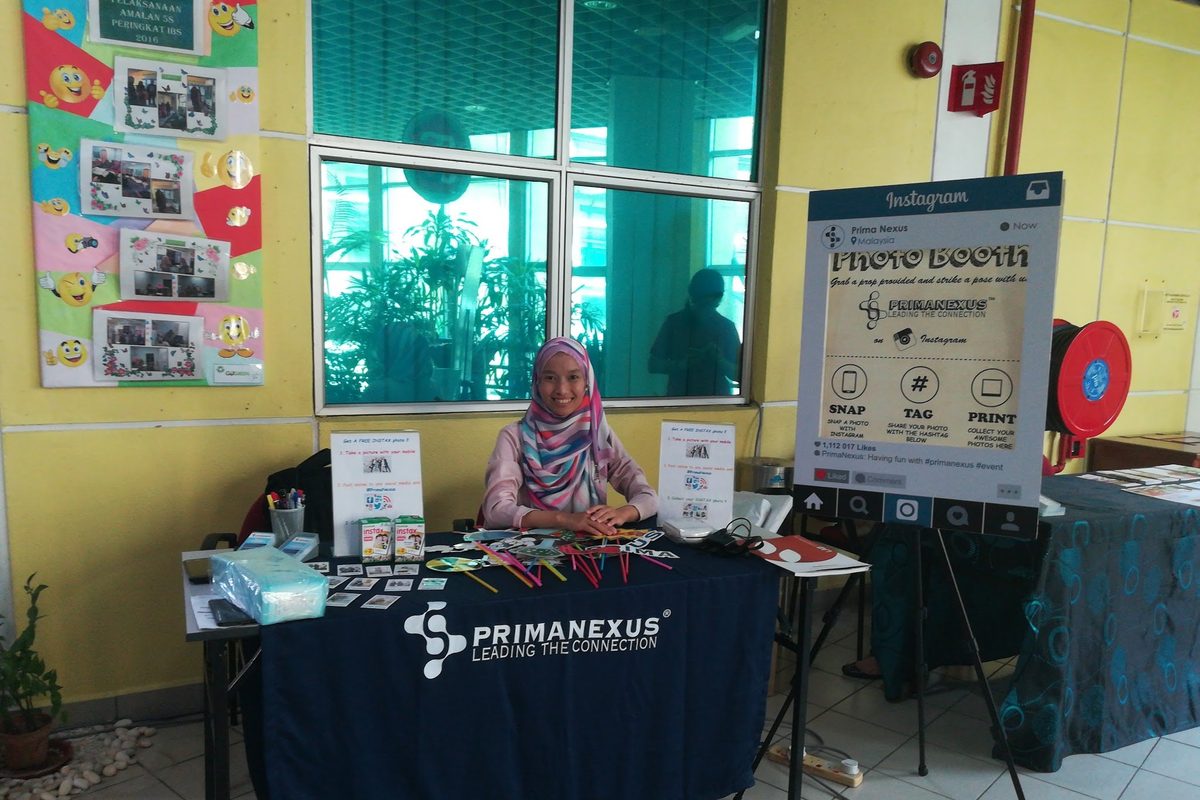 A member of the Prima Nexus team at the Prima Nexus booth, beside a photo booth sign