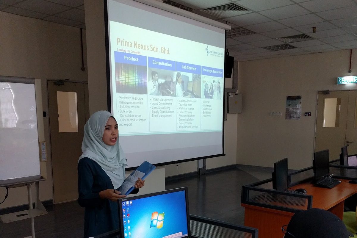 A presenter beside the screen while participants work at computers in the computer laboratory