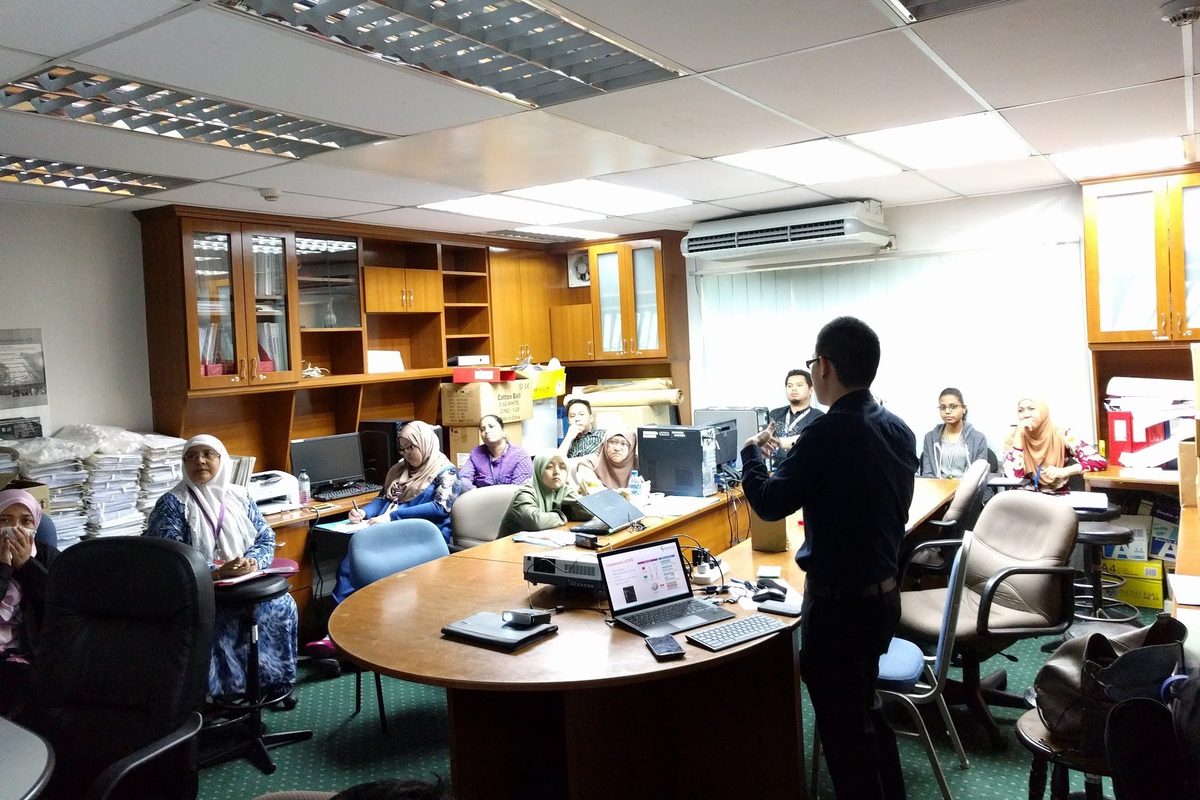 A speaker presents to participants seated around a meeting table