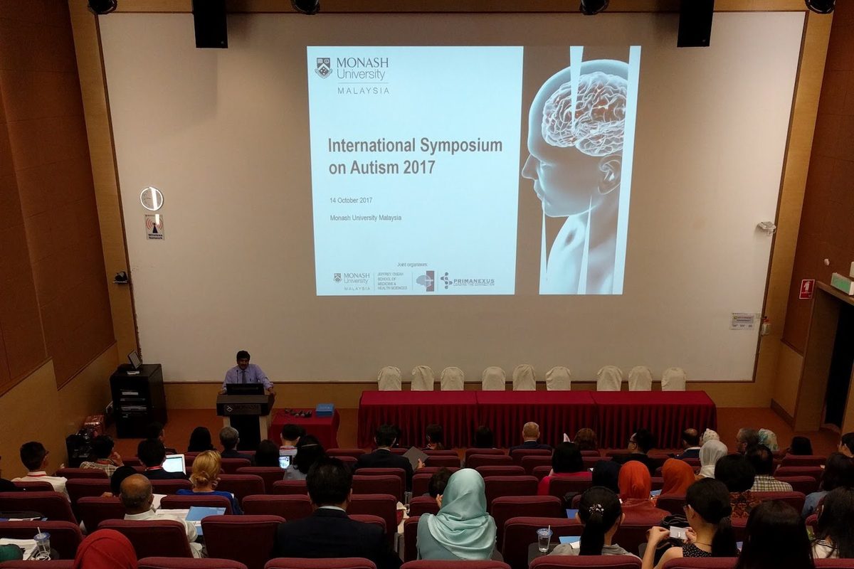 The Plenary Theatre at Monash University Malaysia, with the symposium title on the screen and the audience seated
