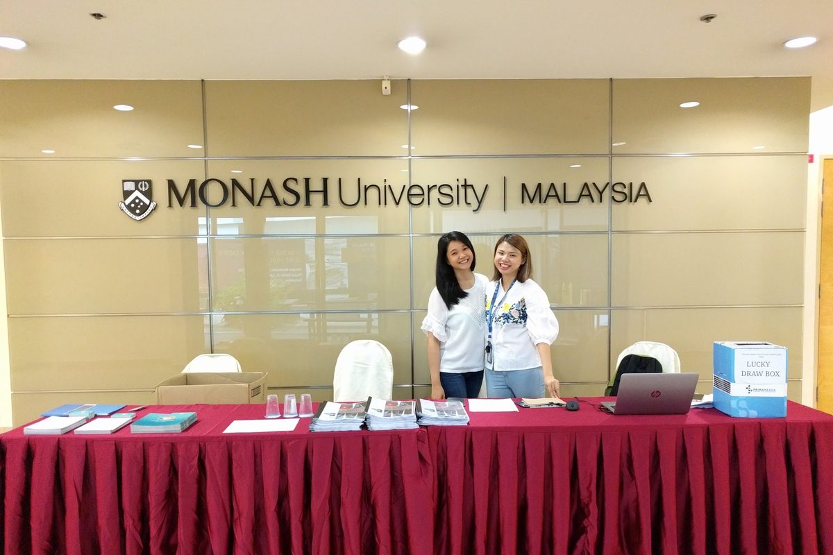 Two members of the organising team at the registration desk under the Monash University Malaysia sign
