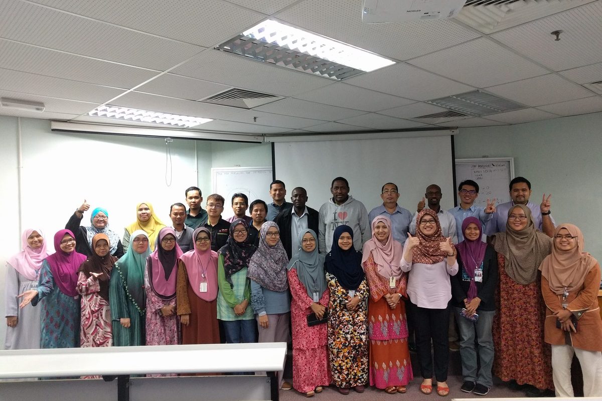 Group photo of the workshop participants standing in rows in front of the screen in a lecture room