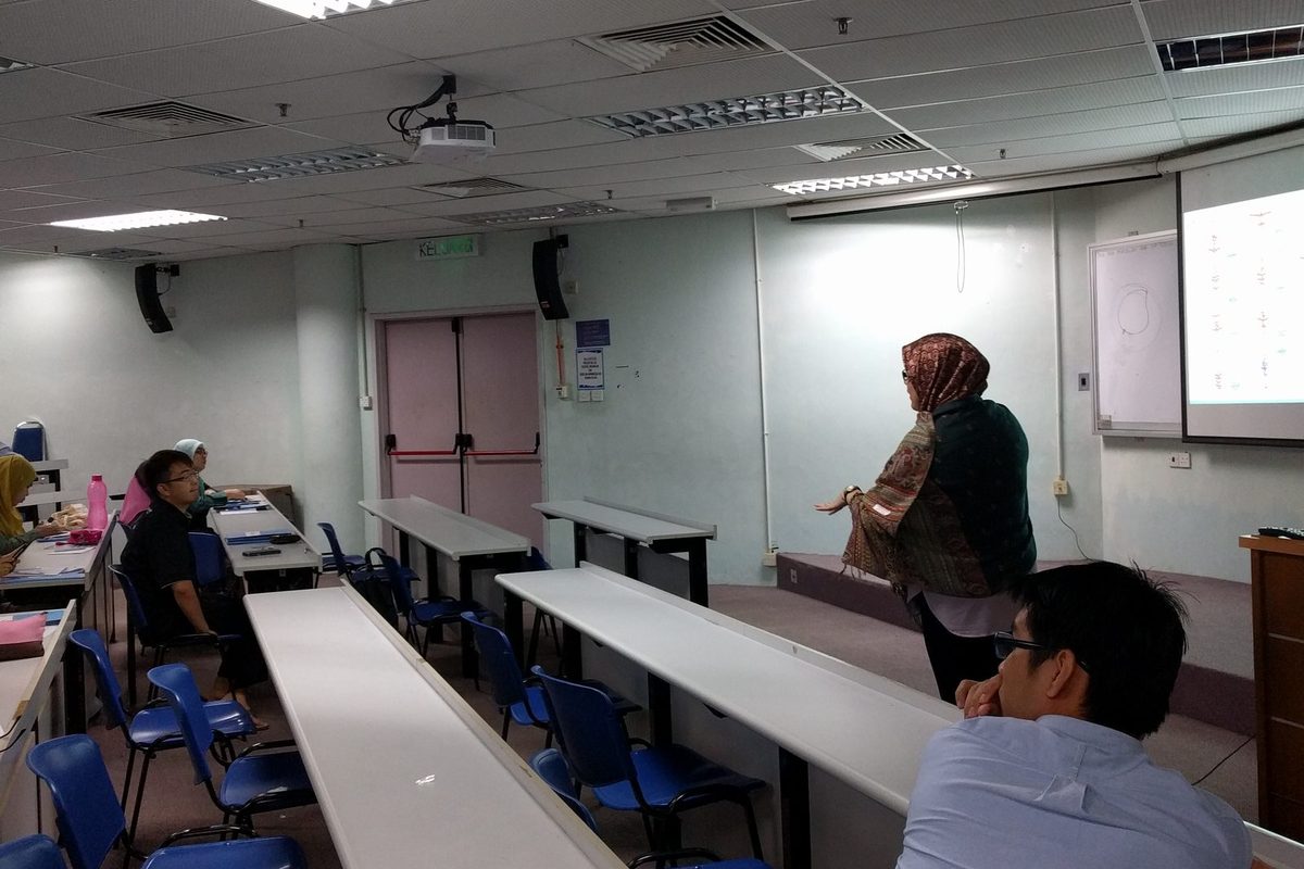 A presenter in a headscarf speaks to participants from the front of the lecture room