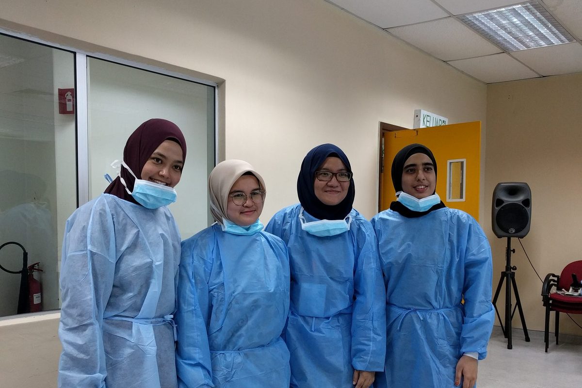 Four participants in blue gowns stand together for a photo in the workshop room