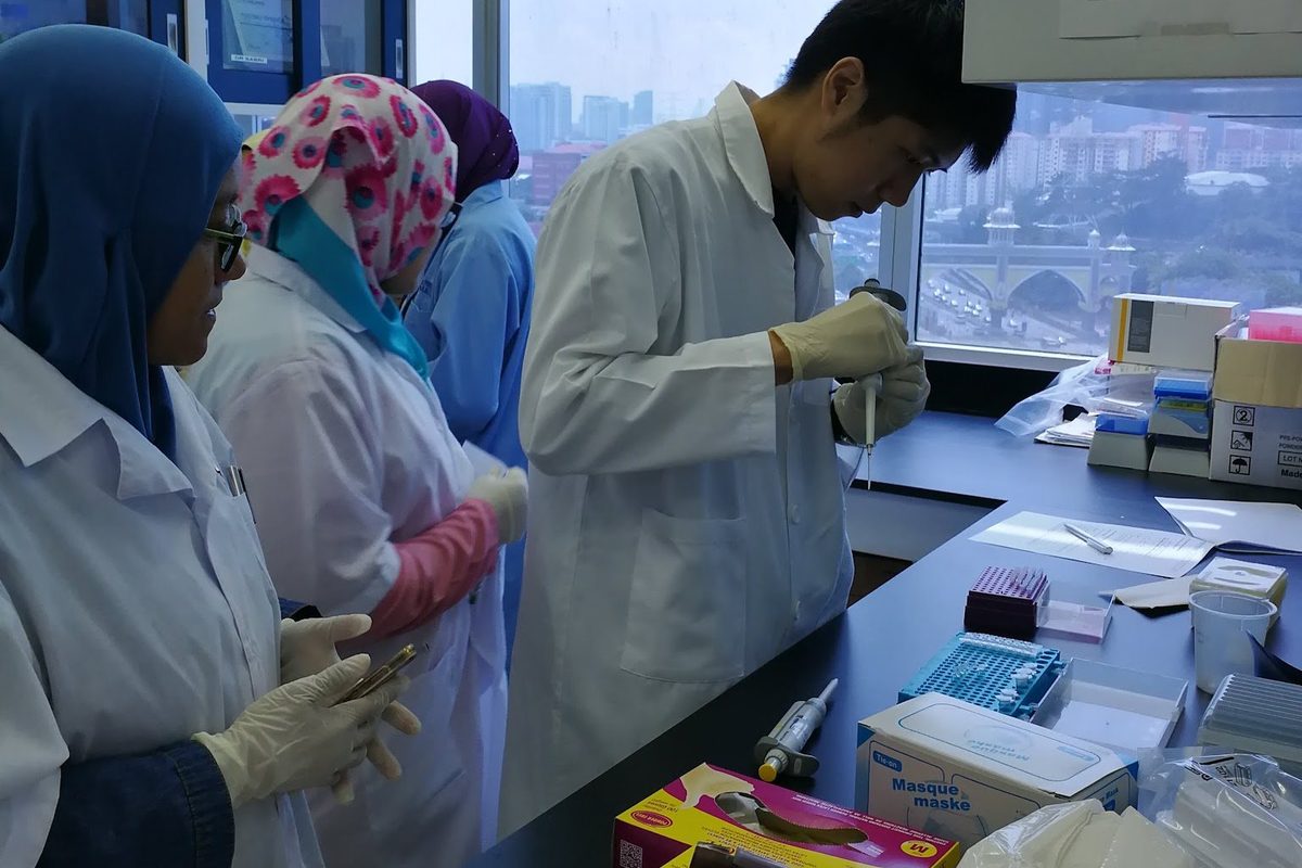 A participant pipettes at the bench while others watch