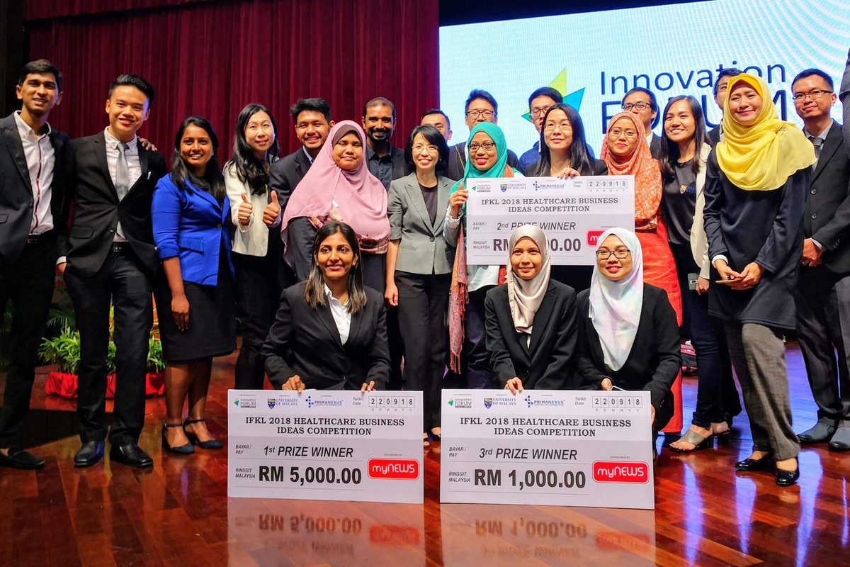 Winners of the IFKL 2018 business ideas competition kneel with large prize cheques in front of organisers and guests, below the Innovation Forum screen
