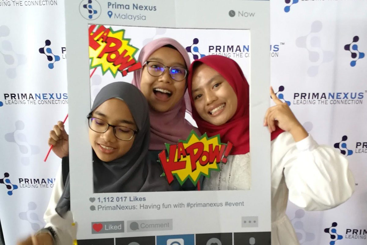 Three participants pose with a photo frame at the Prima Nexus photo wall