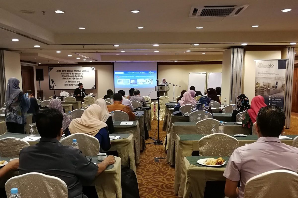 Delegates seated at round tables in a hotel function room, facing the screen