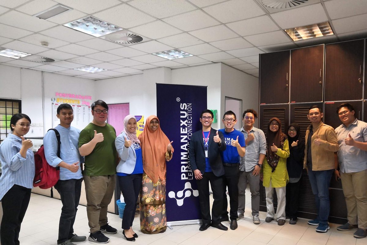 Workshop participants and trainers stand in a row for a group photo beside a Prima Nexus banner
