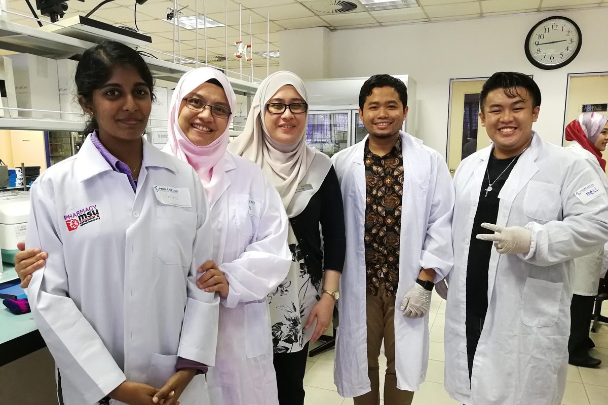 Participants and trainers in lab coats stand together for a group photo in the laboratory