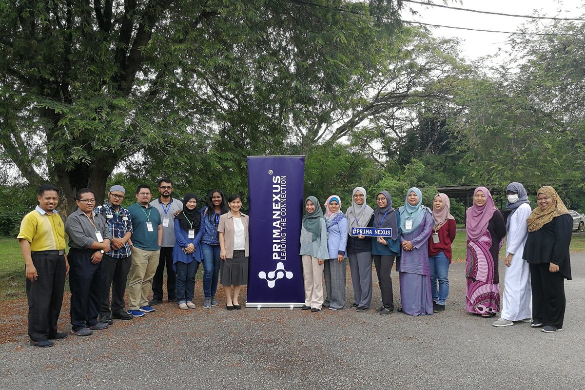 Workshop participants and speakers in a group photo outdoors, beside a Prima Nexus banner