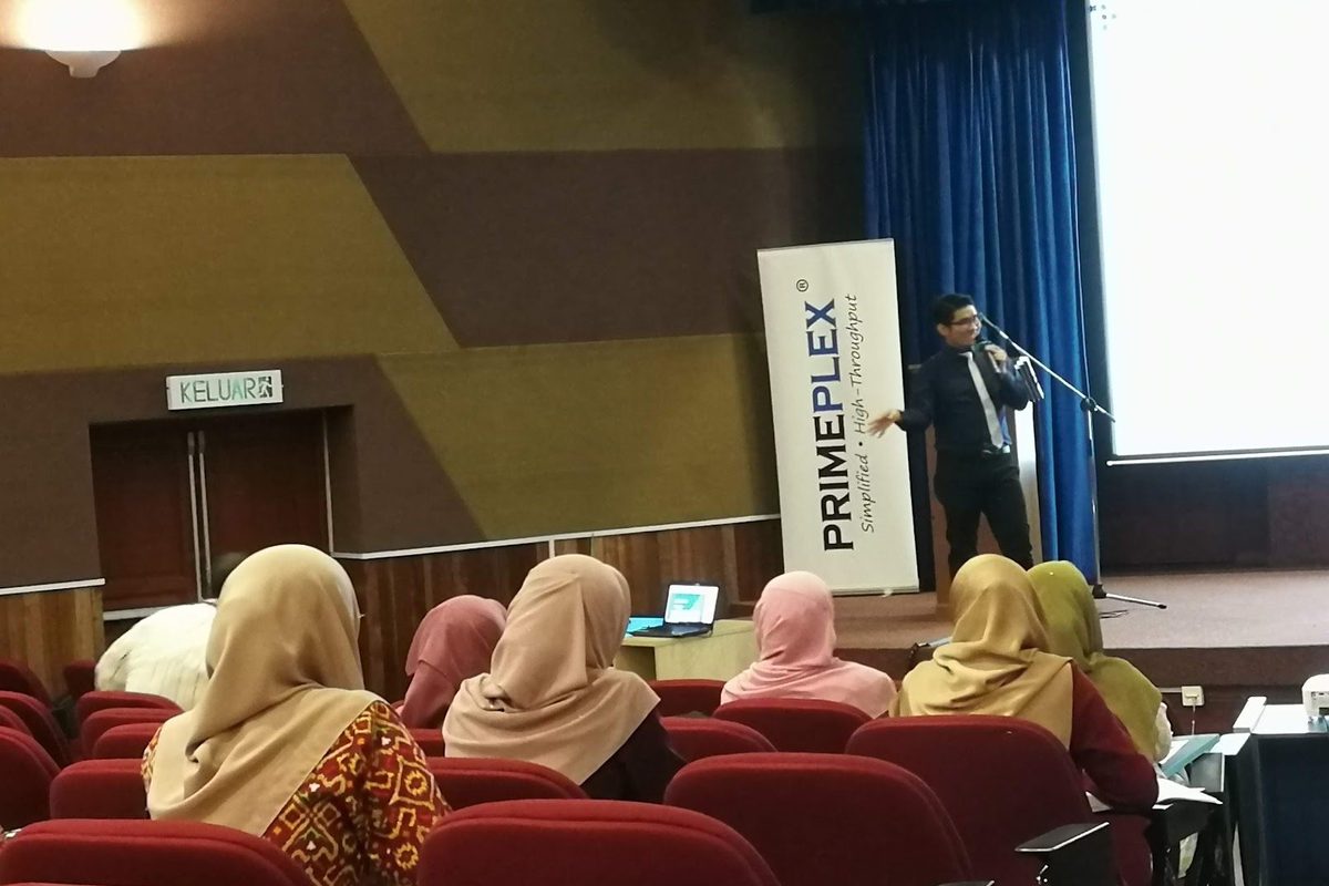 A Prima Nexus representative speaks from the stage of a lecture hall at IIUM Kuantan, with participants seated in the foreground