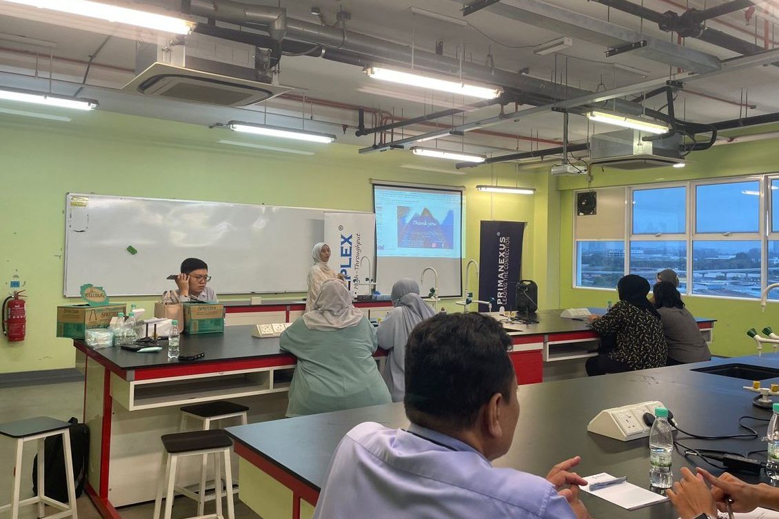 A presenter stands beside the projected closing slide while participants sit at the laboratory benches