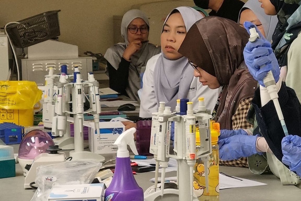 Participants in gloves working at a laboratory bench with reagents and wash bottles